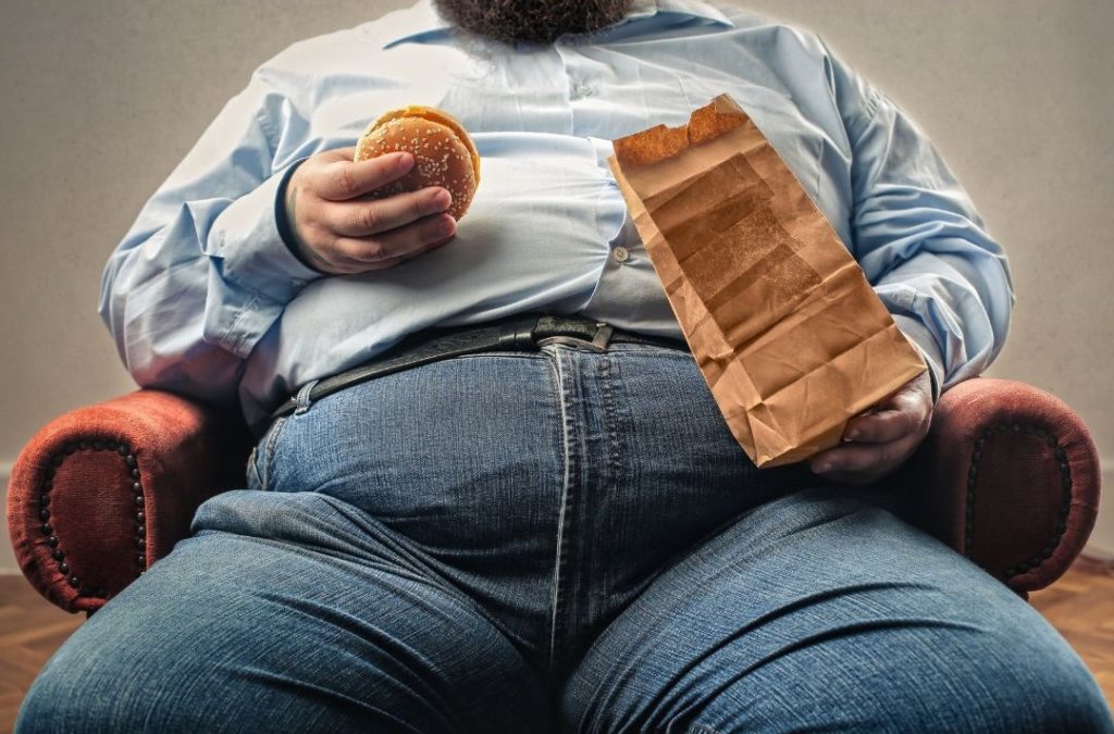 dicker Mann isst Fast Food und ist Risikopatient für Vitamin C Mangel