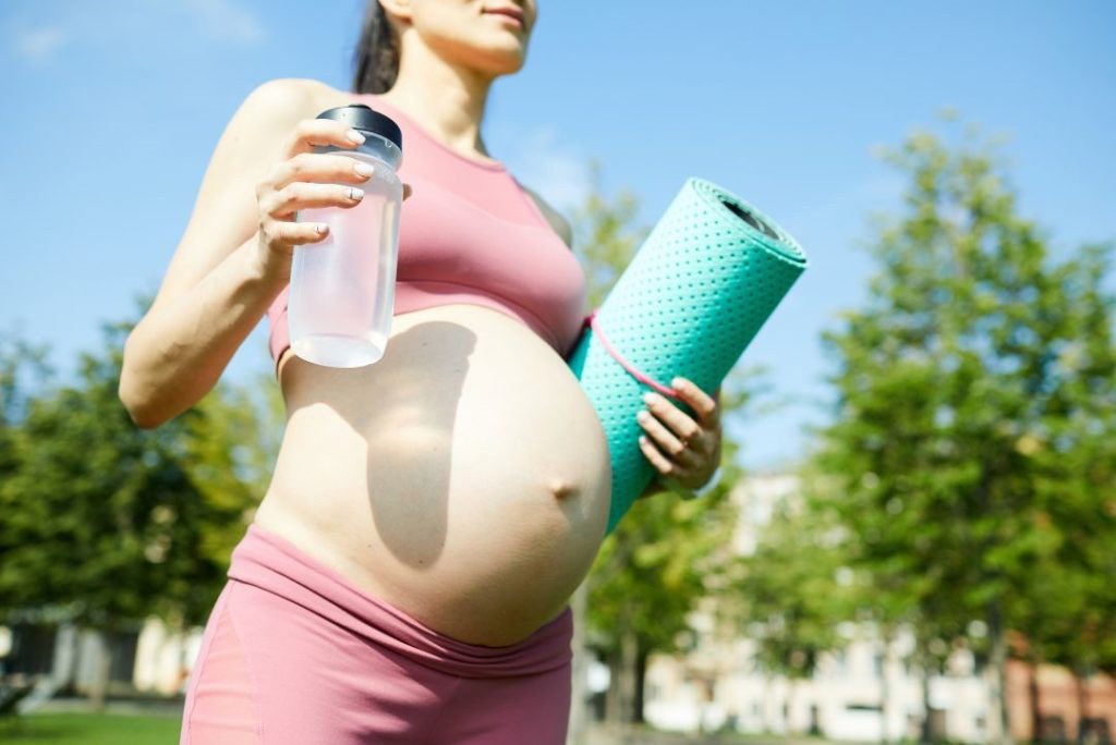 Schwangere outdoor mit Yogamatte und Wasser