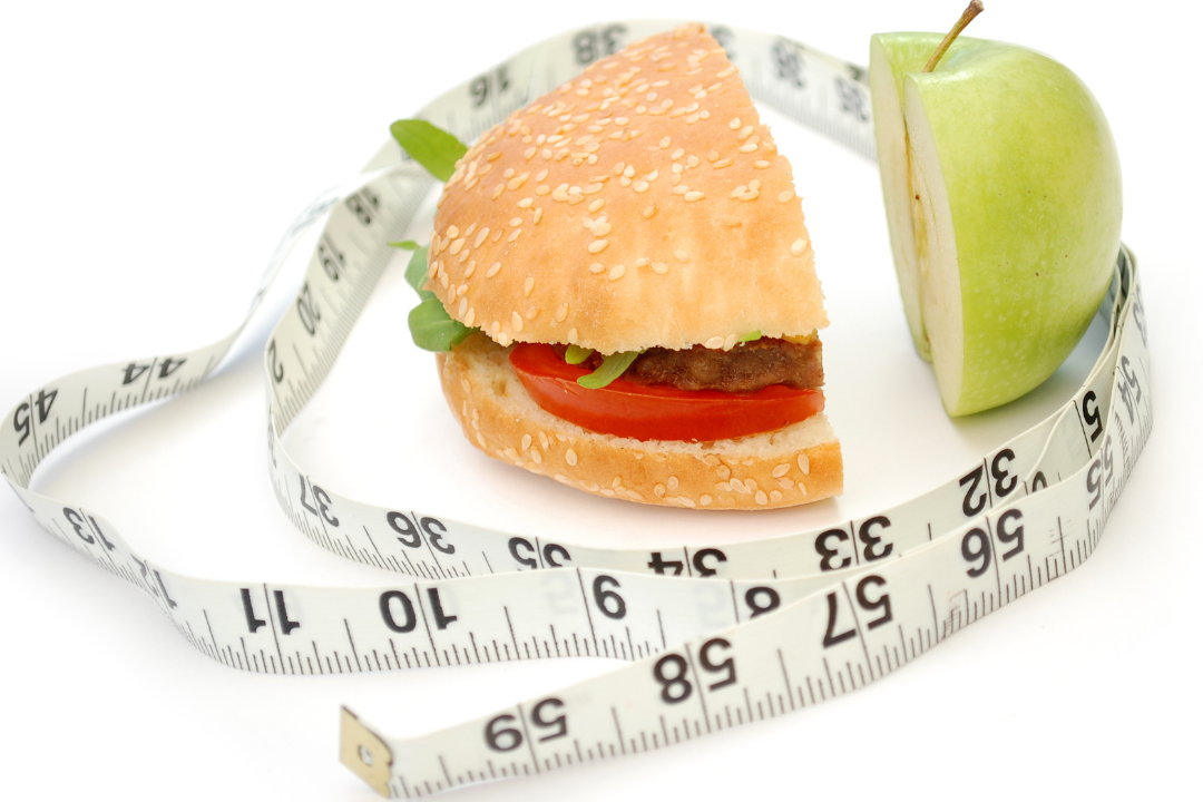 Kalorienbedarf symbolisiert durch Maßband, Apfel und Burger