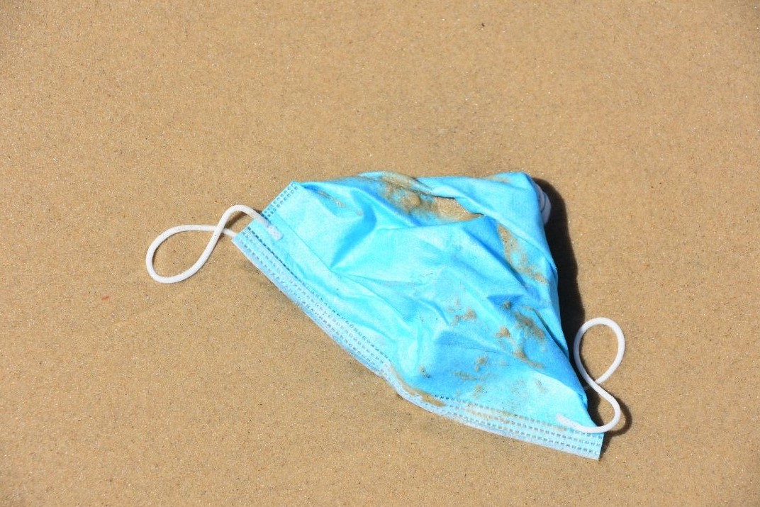 Corona Maske liegt am Strand symbolisch für Post Covid
