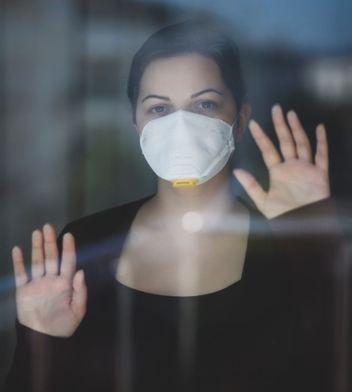 depressive Frau mit Maske am Fenster symbolisch für Post Covid