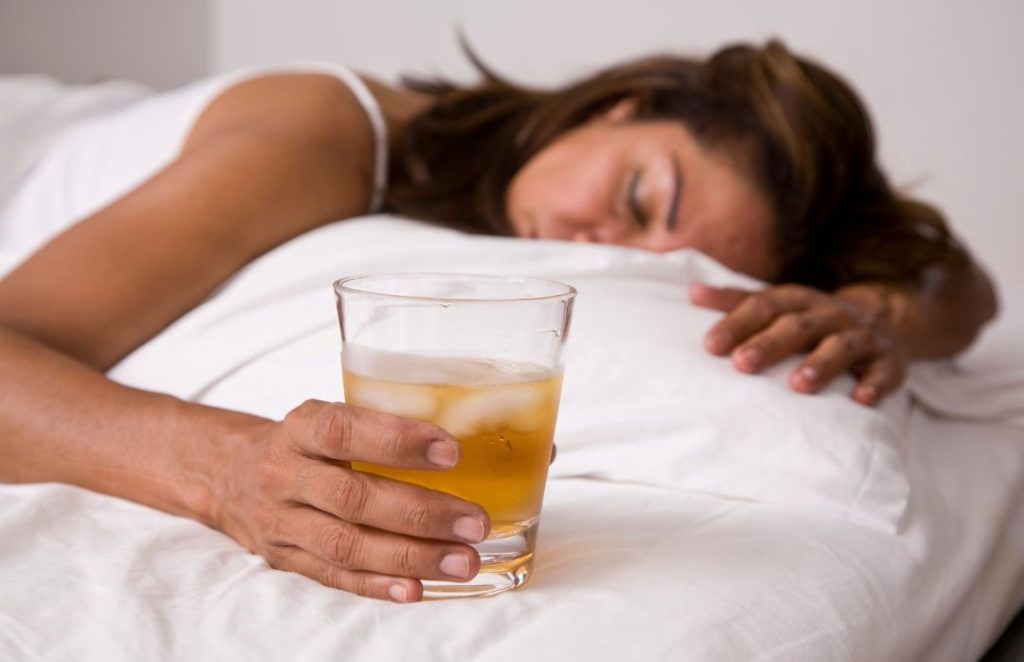 Frau liegt platt im Bett mit Alkohol Glas als Abschreckung für die Leberkur