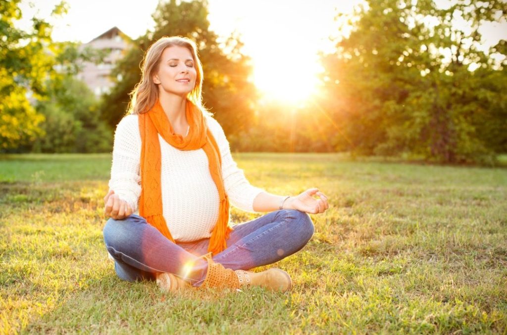 Schwangere sitzt auf Wiese und tankt Vitamin D