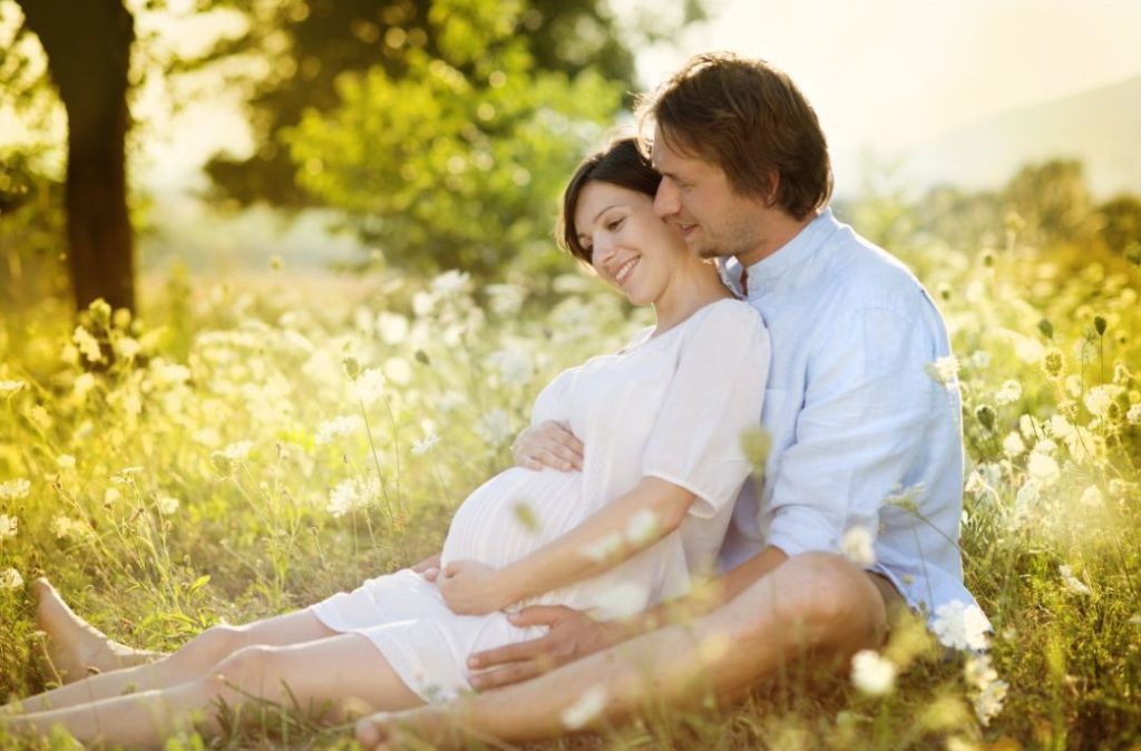 schwangeres Paar auf Wiese tankt Vitamin D durch Sonne und strahlt Kinderwunsch aus