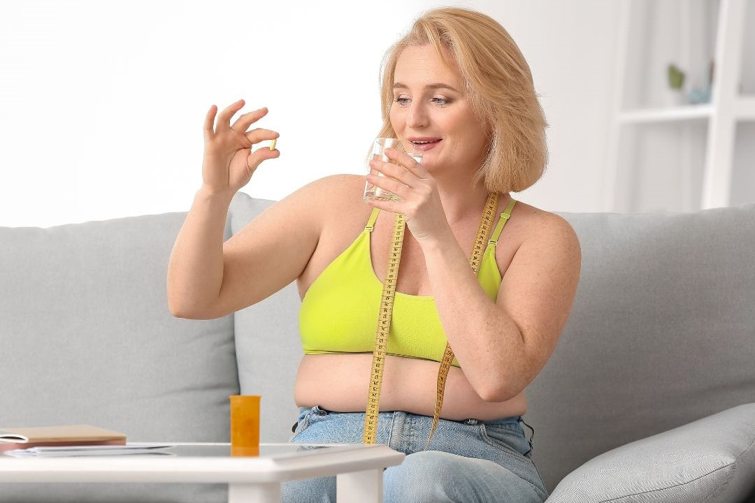 neue Abnehmpille von übergewichtiger Frau in der Hand mit Wasserglas