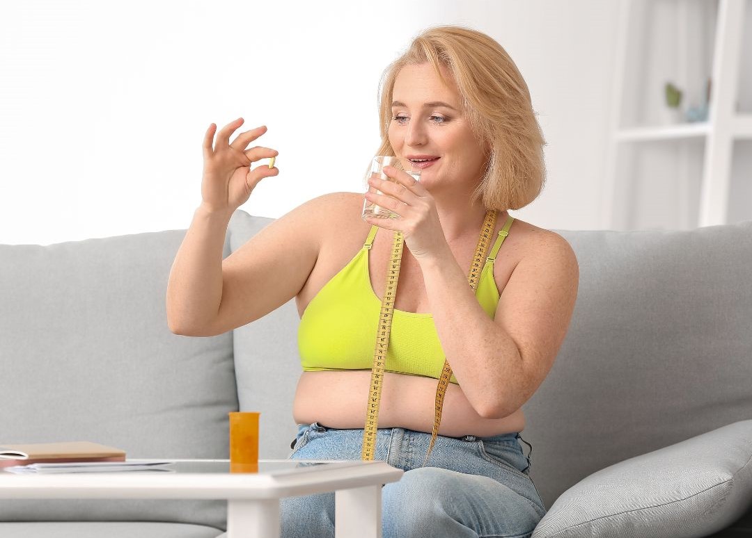 neue Abnehmpille von übergewichtiger Frau in der Hand mit Wasserglas