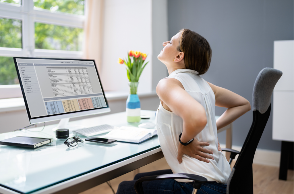 Frau am Schreibtisch zeigt Rückenschmerzen durch verkürzten Hüftbeuger