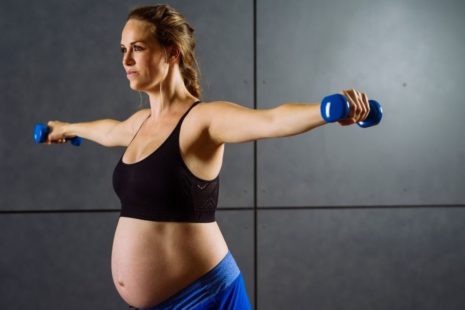 Sport für Schwangere dargestellt von Frau mit Kurzhanteln und Bauch