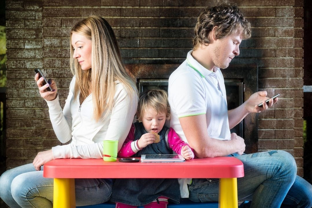 Bewegungsmangel dargestellt von junger Familie am Tisch mit Handys